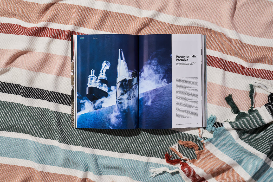 a copy of gear patrol magazine on a striped beach blanket open to the story Paraphenalia Paradox with a large visual of bongs and smoke