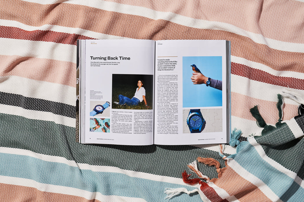 a copy of gear patrol magazine on a striped beach blanket open to the story Turning Back Time with photos of a woman and several colorful watches