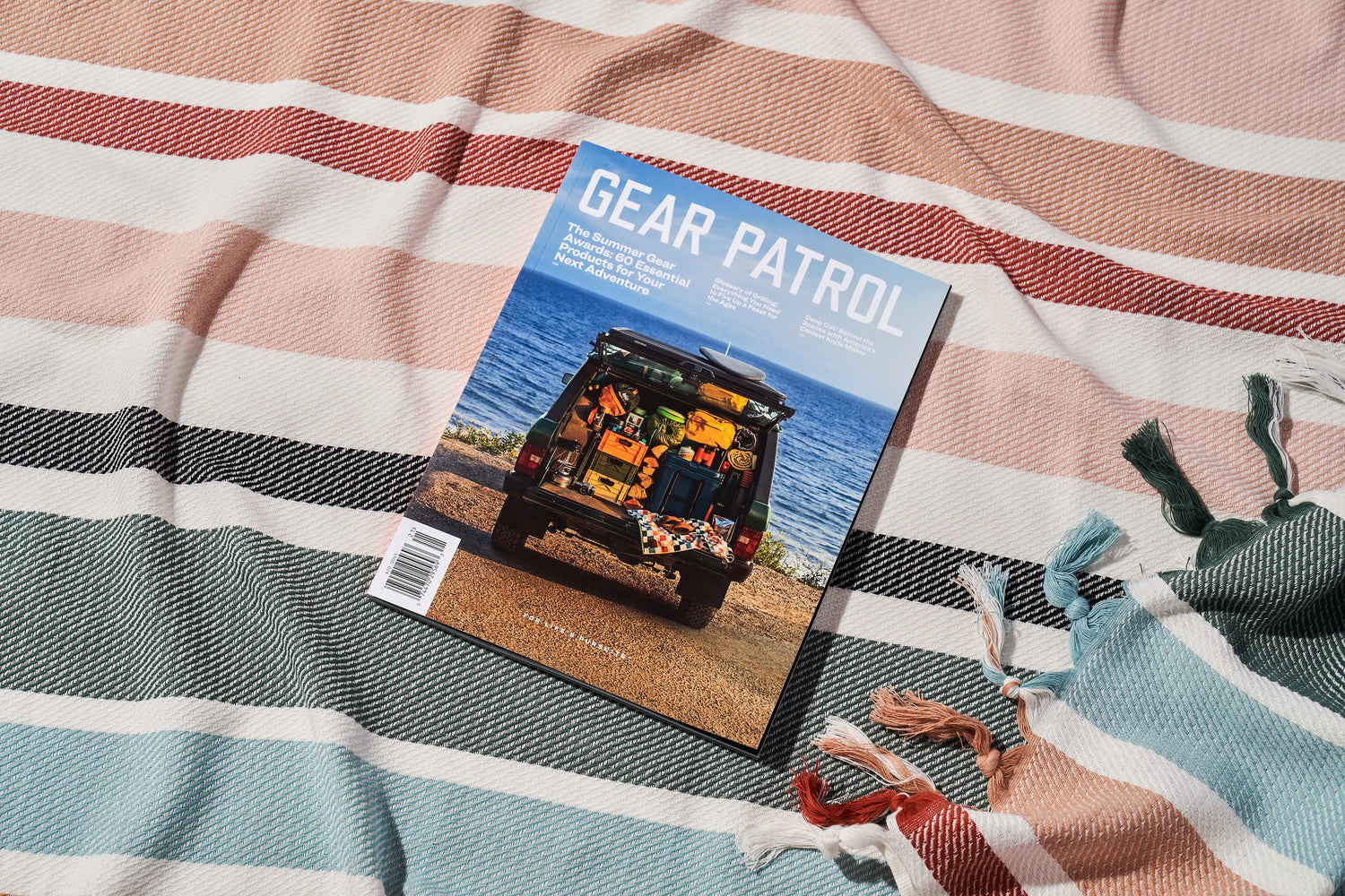 gear patrol magazine, issue eighteen laying on a colorful striped beach blanket