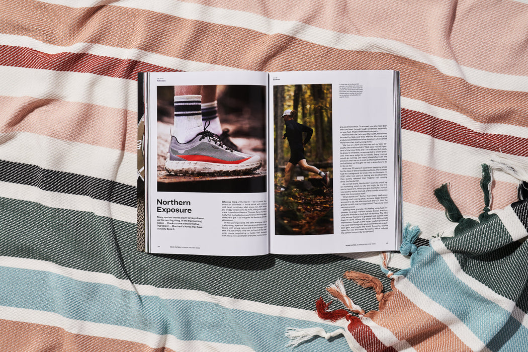 a copy of gear patrol magazine on a striped beach blanket open to the story Northern Exposure with photos of running shoes and a man running