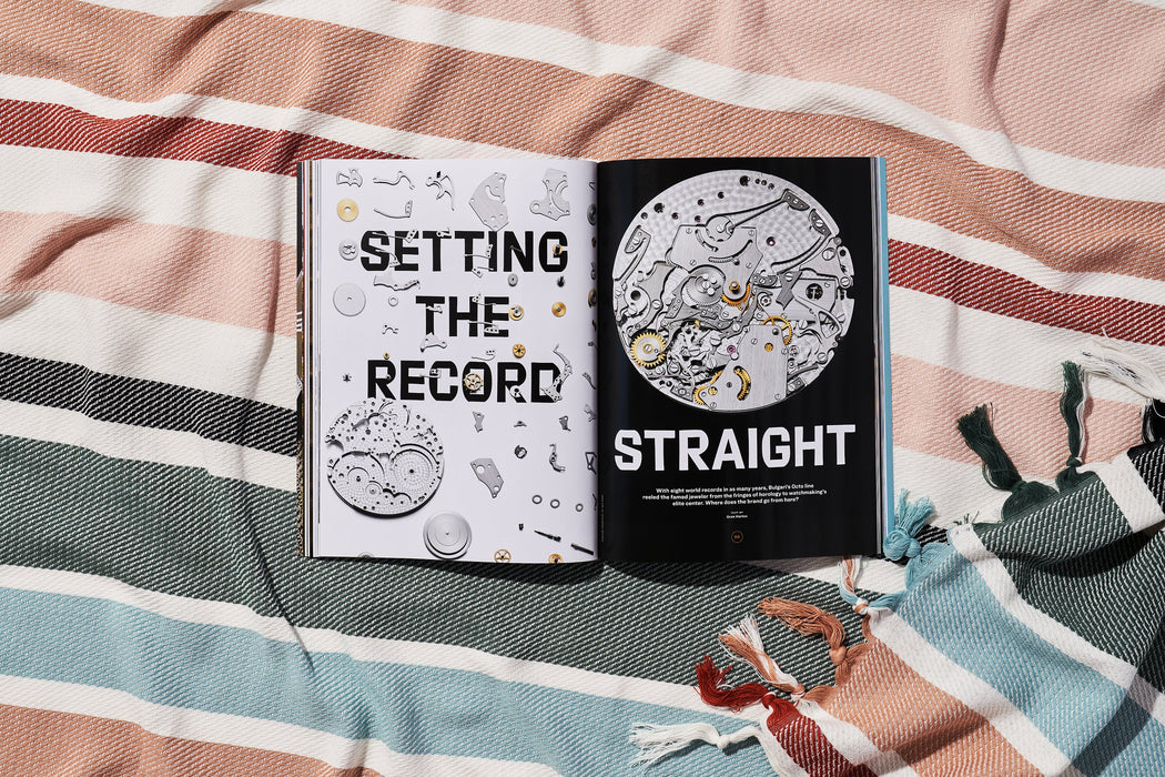 a copy of gear patrol magazine on a striped beach blanket open to the story setting the record straight with visuals of watch gears and pieces 